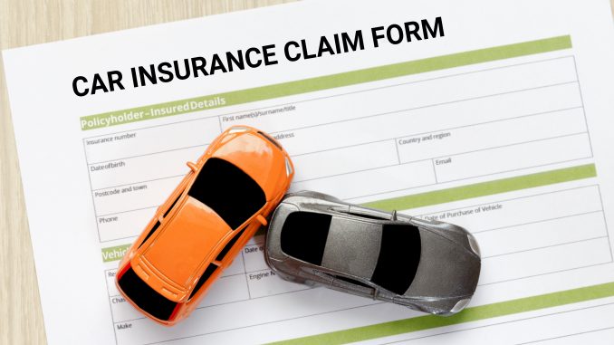 Top view of car insurance claim form with car toy crash on wooden desk.